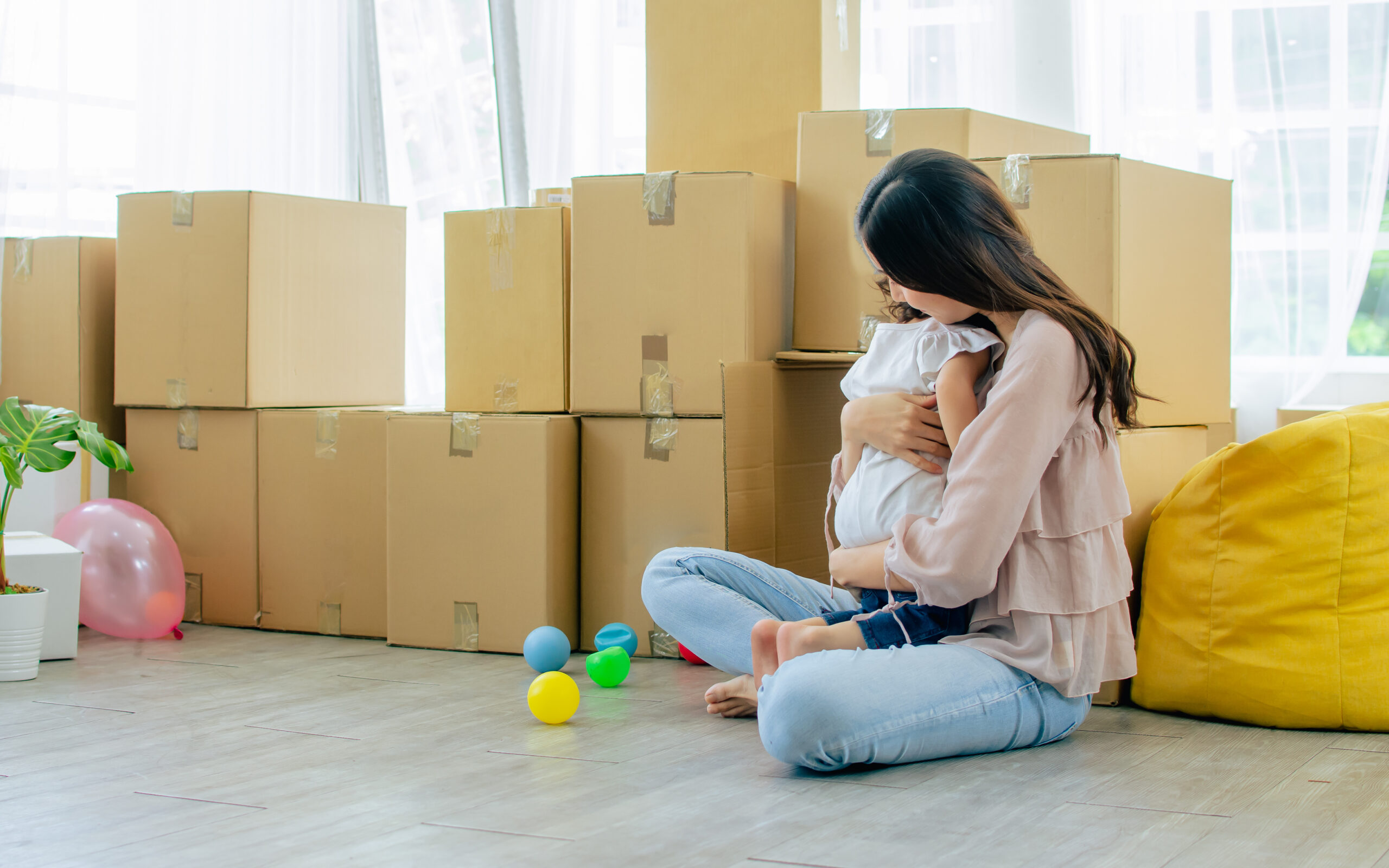 Mother, Little cute Caucasian girl with curly hair sitting on floor in living room, playing toys together with fun, warm hug with love, happiness in house with aper carton boxes for moving new home